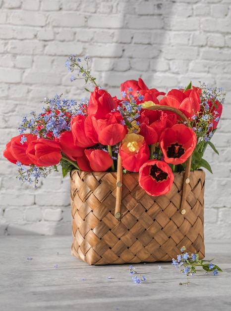 Photo summer or spring bouquet of daffodils and red tulips in a wicker basket located on a white surface