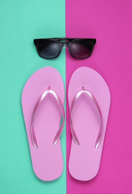 Фото Летний натюрморт. пляжные аксессуары. модные пляжные розовые шлепки, солнцезащитные очки на розовом синем бумажном фоне.