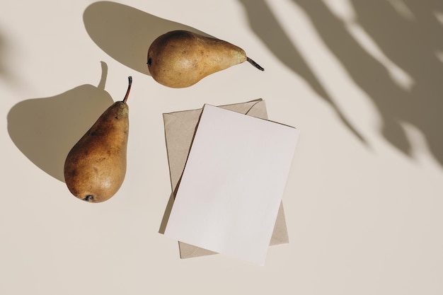 Summer still life composition Autumn weddding greeting card envelope mock up scene Two pears fruit long harsh shadows overlay Beige table background in sunlight Flat lay top view no people