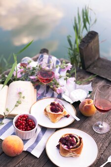 Estate still life- picnic su un molo in legno. vino, sinabones, pesche, un libro vista lago