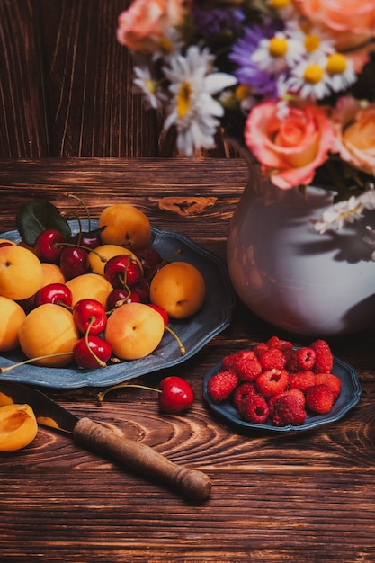 Summer still life with peaches, raspberries, cherries and flowers on a wooden table