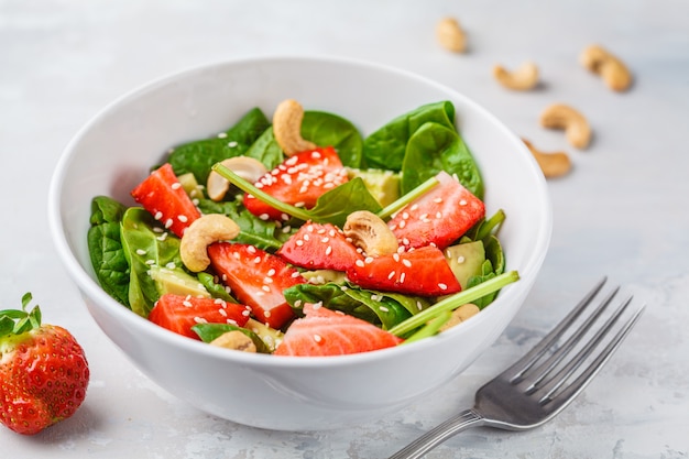 Summer strawberry avocado salad with cashews in a white bowl. 