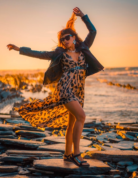 Summer street style on a beach next to rocks of a young brunette caucasian woman in a leopard dress by the sea Sakoneta beach in the town of Deba Basque Country Looking to the right