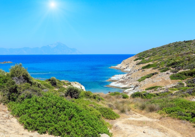 遠く（ハルキディキ、シトニア、ギリシャ）のアトスマウントビューと夏の日当たりの良い石の多い海岸の風景。