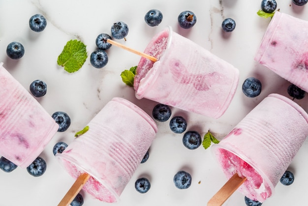 Dolci e dessert estivi. cibo vegano. bevande congelate, frullati. ghiaccioli di gelato da yogurt greco fatto in casa e mirtilli biologici freschi. alla menta sul tavolo di marmo bianco. copia spazio vista dall'alto