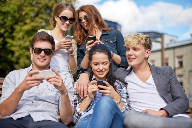 summer, technology, education and teenage concept - group of happy students or teenagers with smarphones taking selfie and texting messages at campus