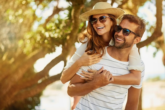 夏の彼らは永遠に覚えている夏の日の屋外でピギーバックライドを楽しんでいる幸せな若いカップルのショット