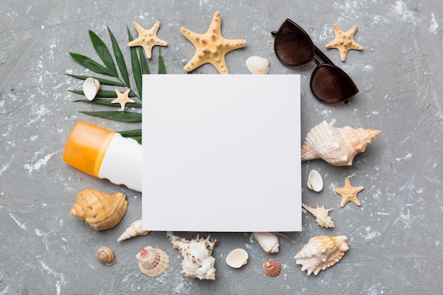 Photo summer time concept with blank greeting card and blank white paper on colored background seashells from ocean shore in the shape of frame separated with space for text top view