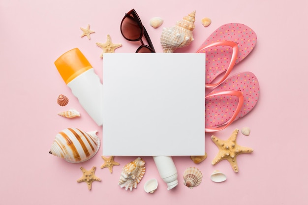 Summer time concept with blank greeting card and blank white paper on colored background Seashells from ocean shore in the shape of frame separated with space for text top view