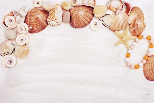 Summer time concept with seashells, star, sea pebbles, womens bracelet on white sand with copy space.