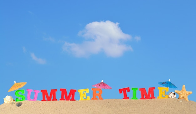 Summer time letters on a beach sand against the blue sky