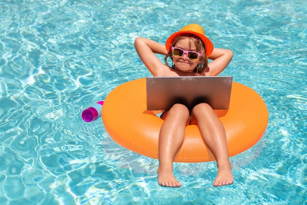 Bambino di concetto di viaggio e affari estivo con il computer portatile nell'acqua della piscina nel computer portatile impermeabile di giorno d'estate