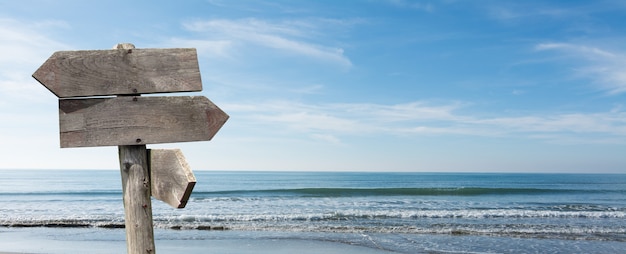 Summer travel destinations options. Direction road sign with wooden arrows on beach and sea