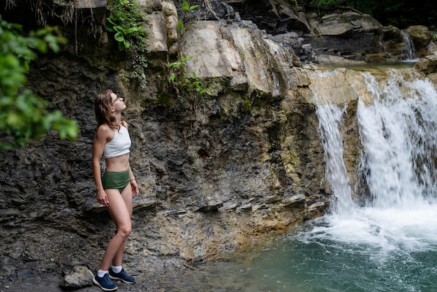 夏の旅行。滝を魅了する水着姿のセクシーな女性。滝の前の女性