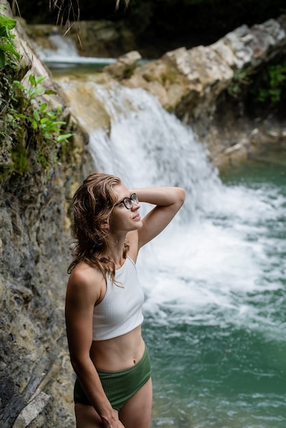 Summer travel. Young sexy woman in swimsuit enjoing the waterfall.