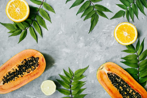 Summer tropical composition green leaves and tropical fruits papaya orange lemon on gray background