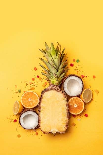 Summer tropical fruits with orange, lemon, pineapple on a pastel yellow background.