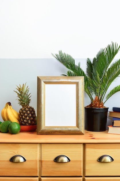 Foto concetto di interni tropicali estivi, cornice con uno spazio vuoto in piedi su una cassettiera progettata da una scuola antica decorata con palme tropicali in una pentola e frutti tropicali in un piatto