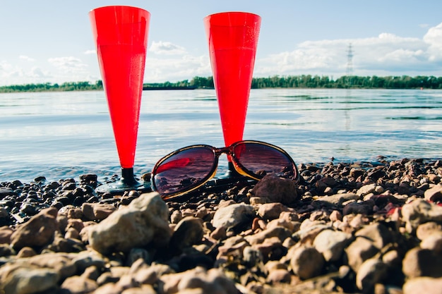 In the summer two red glasses of sparkling champagne or prosecco in the bay and sunglasses on a pebbly beach