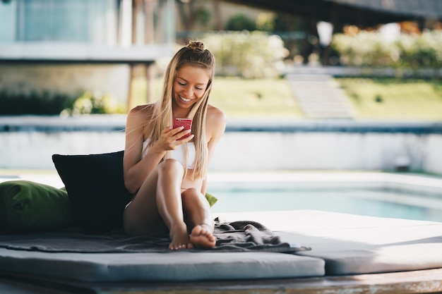 Summer vacation beach luxury resort hotel holiday tropical rest background young beautiful happy sexy Caucasian smiling girl relaxing near pool lounger reading chat in mobile phone