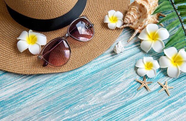 Concetto di vacanza estiva. cappello di paglia e accessori da spiaggia con conchiglie e stelle marine su fondo di legno blu