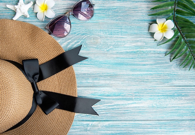 Summer vacation concept. Straw hat and frangipani flowers on blue wooden background