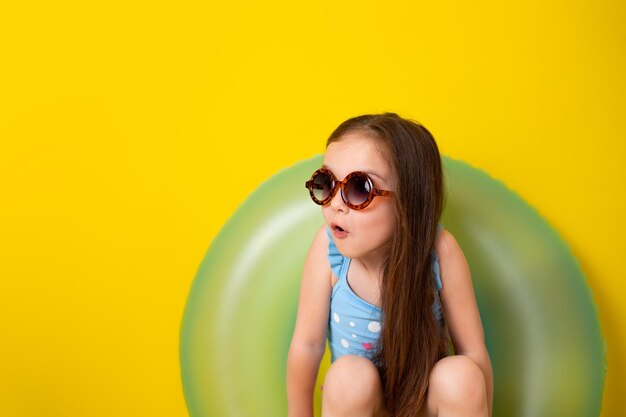 Summer vacation A cute girl in sunglasses and a swimsuit circle yellow background Space for text