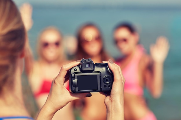 summer vacation, gesture, technology, travel and people concept - close up of smiling young women photographing by camera and waving hands on beach