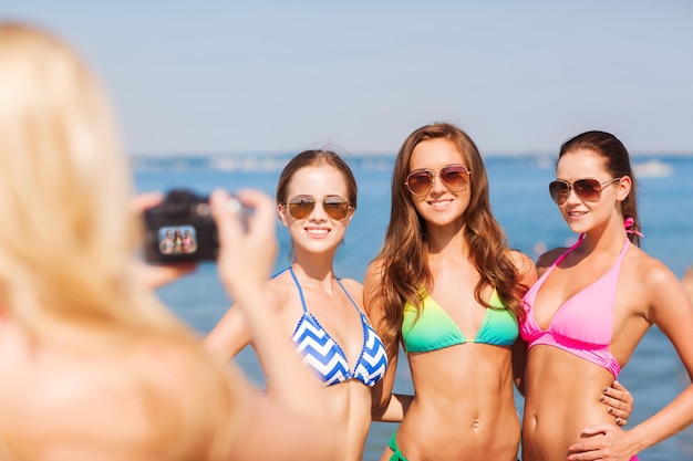 летние каникулы, жесты, путешествия и концепция людей - группа улыбающихся молодых женщин, фотографирующих на камеру и машущих руками на пляже
