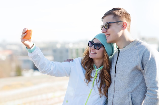 summer, vacation, holidays, technology and friendship concept - smiling couple with smartphone taking selfie outdoors