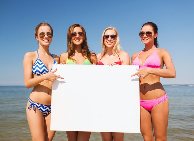 summer vacation, holidays, travel, advertising and people concept - group of smiling young women with big white blank billboard on beach