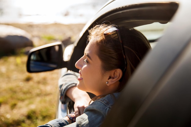 summer vacation, holidays, travel, road trip and people concept - happy smiling teenage girl or young woman in car at seaside