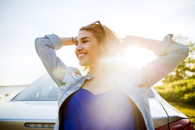 Foto vacanze estive, vacanze, viaggi, viaggio su strada e concetto di persone - adolescente sorridente felice o giovane donna vicino all'auto in riva al mare