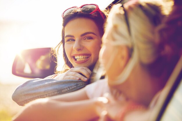 summer vacation, holidays, travel, road trip and people concept - happy teenage girls or young women in car at seaside