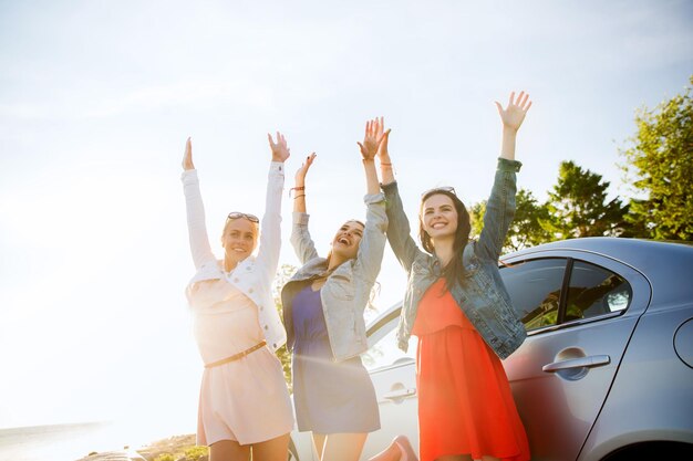 summer vacation, holidays, travel, road trip and people concept - happy teenage girls or young women near car at seaside