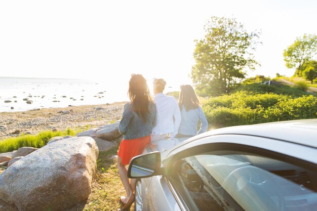 Foto vacanze estive, vacanze, viaggi, viaggio su strada e concetto di persone - adolescenti felici o giovani donne vicino all'auto in riva al mare