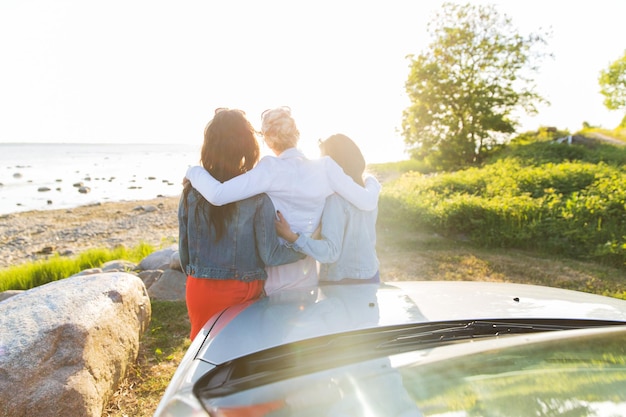 summer vacation, holidays, travel, road trip and people concept - happy teenage girls or young women near car at seaside