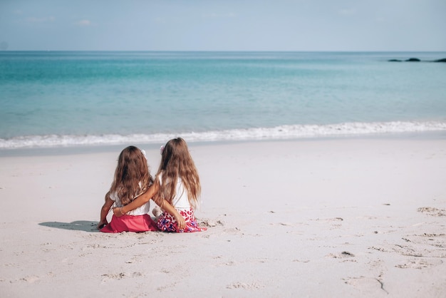 Летний отпуск. Маленькие девочки сидят на песчаном пляже и смотрят на синее море и небо. Концепция путешествий, отдыха и приключений