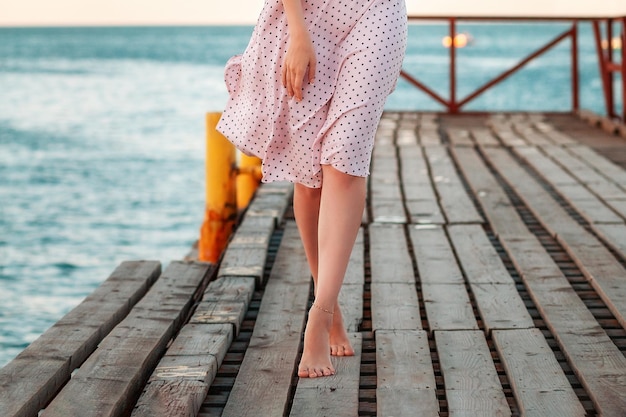 Summer vacation a slim woman in a dress is walking on tiptoe along the pier by the sea legs close up