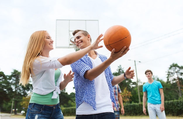 Photo summer vacation, sport, games and friendship concept - group of happy teenagers playing basketball outdoors