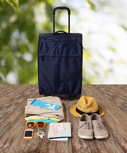 summer vacation, tourism and objects concept - travel bag, map, air ticket and clothes with personal stuff over wooden floor and nature background