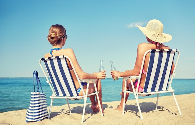 Vacanze estive, viaggi e concetto di persone - donne felici che bevono birra e prendono il sole nei salotti sulla spiaggia