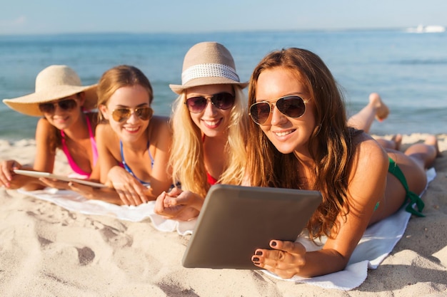 summer vacation, travel, technology and people concept - group of smiling women in sunglasses with tablet pc computers lying on beach