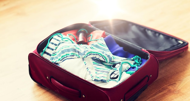 여름 휴가, 여행, 관광 및 물체 개념 - 해변 옷, 선글라스, 자외선 차단제로 여행용 가방 가까이