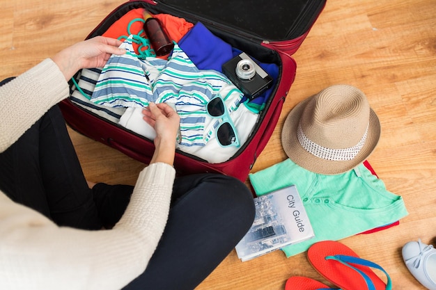 летние каникулы, путешествия, туризм и концепция объектов - крупный план женщины, упаковывающей дорожную сумку в отпуск