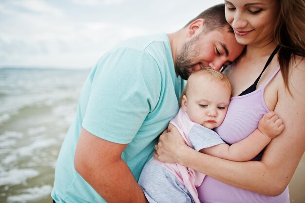 夏休み。親と子供との野外活動。幸せな家族の休日。父、妊娠中の母親、海砂浜の赤ん坊の娘。