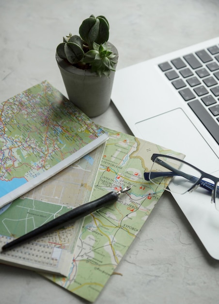 Summer vacations planning laptop computer old map pot plant and\
glasses on light background travel and wandelust concept selective\
focus