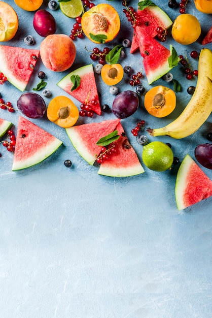 Foto estate concetto di cibo vitaminico, vari frutti e bacche anguria pesca menta prugne albicocche ribes mirtillo, creativo piatto disteso su sfondo azzurro vista dall'alto copia spazio