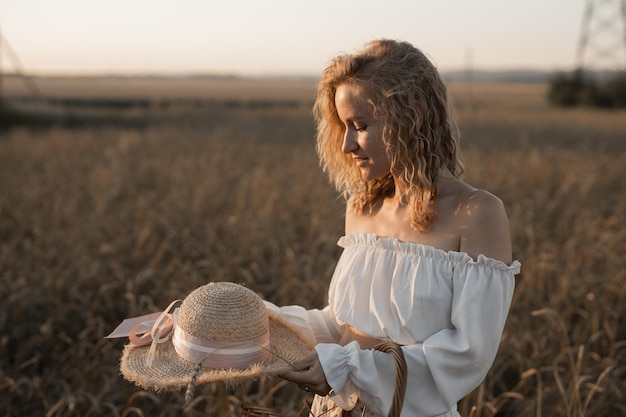 Foto passeggiata estiva di una bella giovane donna con un cappello attraverso un campo al tramonto