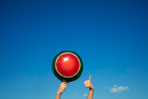 Summer watermelon balloon held in the air against a bright blue summer sky